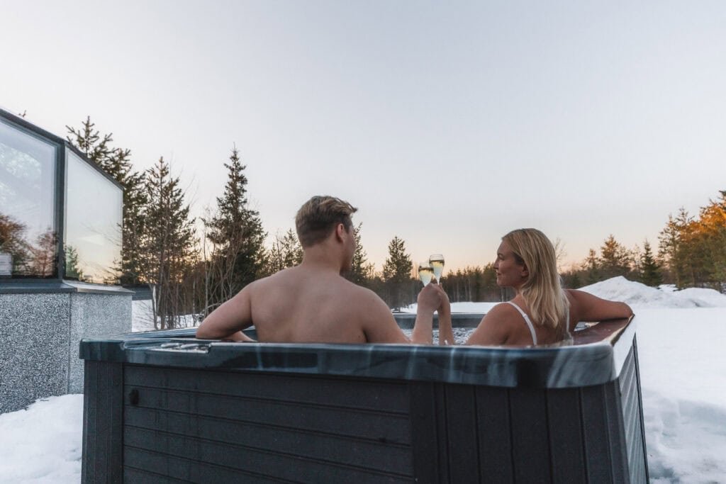 Couple in an outdoor hot tub beside a glass igloo