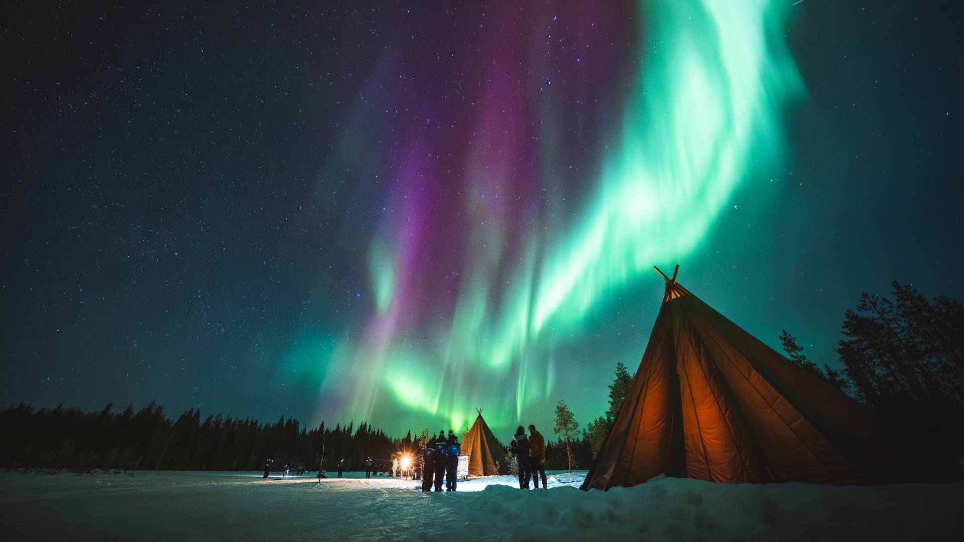 Glowing kota tepees under green and purple Northern Lights