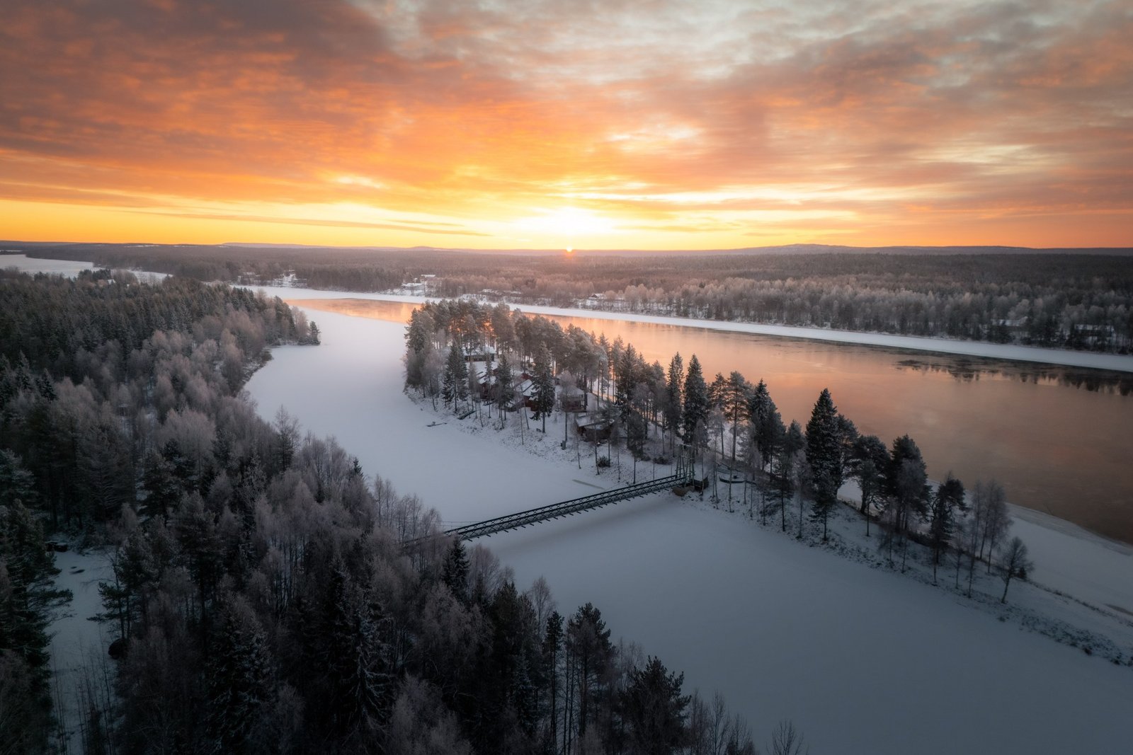 Aerial view of a frozen river and forest at sunset near Rovaniemi